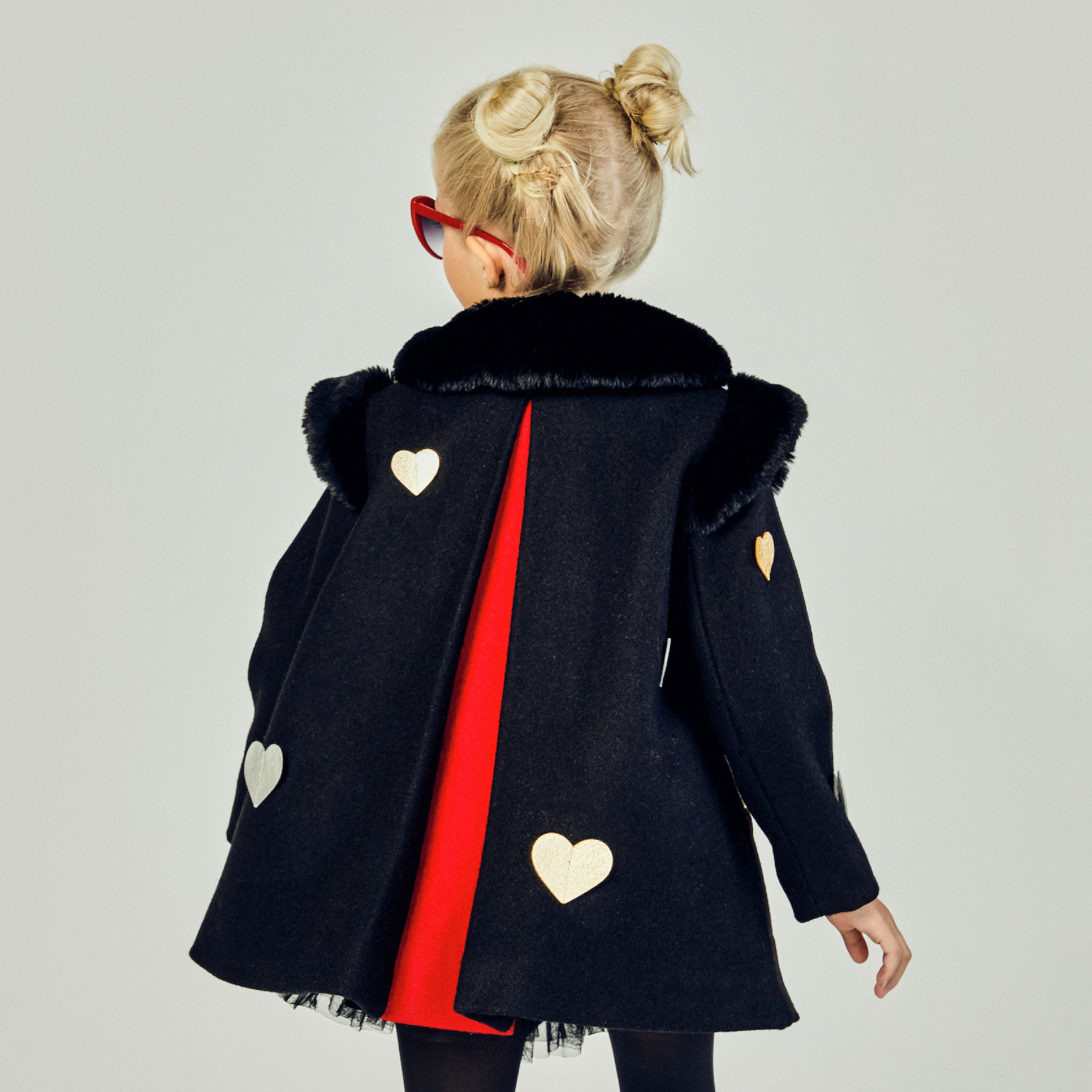 Back view of black girls' winter coat with faux fur collar, gold and silver heart appliqués, and red pleated lining