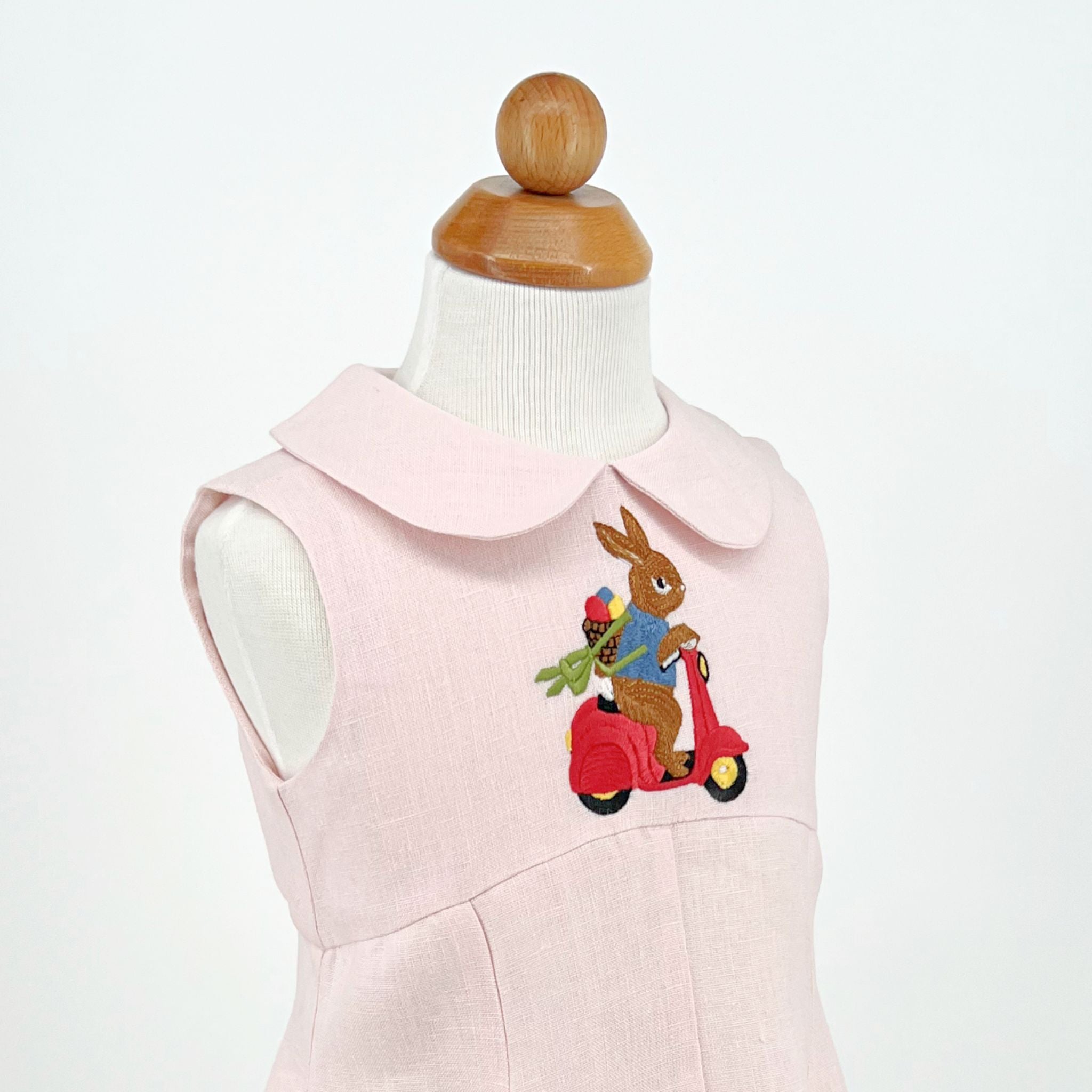 Close-up of Little Goodall Blush Linen Scooter Bunny Dress, showing embroidered bunny on red scooter with basket of vegetables