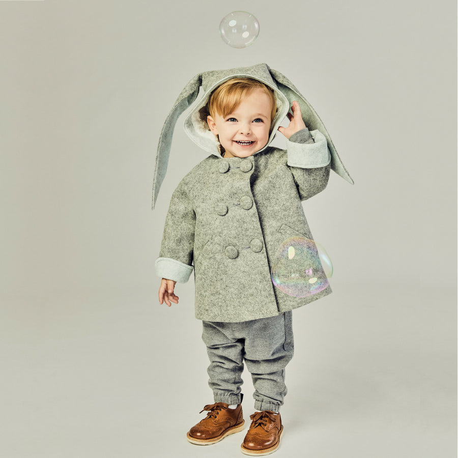Smiling boy wearing grey bunny coat with hood up, revealing plush lining. One ear flops down while the other is lifted. Double-breasted buttons 