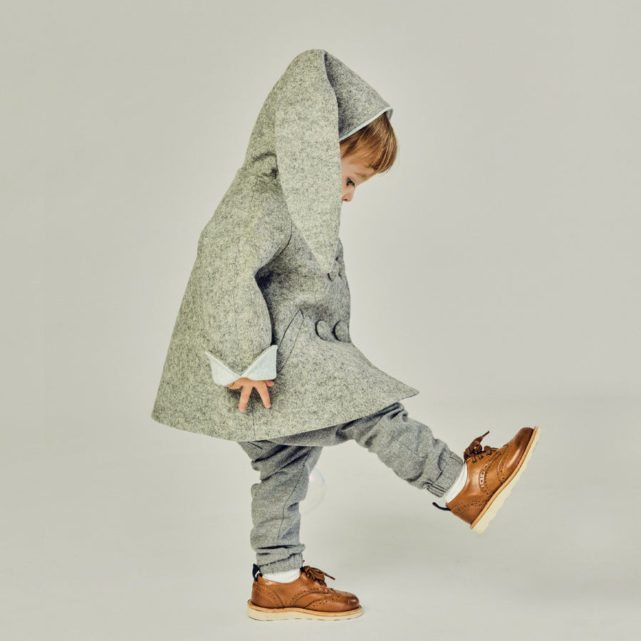 Side view of a child in a grey wool bunny coat with light blue lining, lifting a foot in motion. 