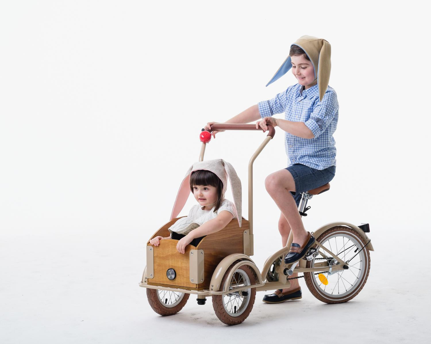 Little boy model wears a tan bunny hat while stirring the bikewagon. The little girl is modeling the oatmeal bunny hat while sitting in the wagon.