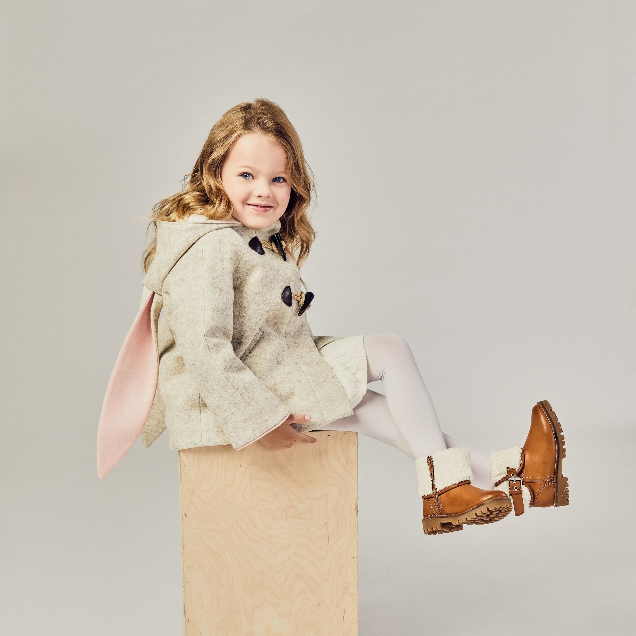 girl wearing the Little Goodall Snowshoe Rabbit Coat – a merino wool jacket with bunny ear hood, toggle fasteners, and plush faux fur lining for kids