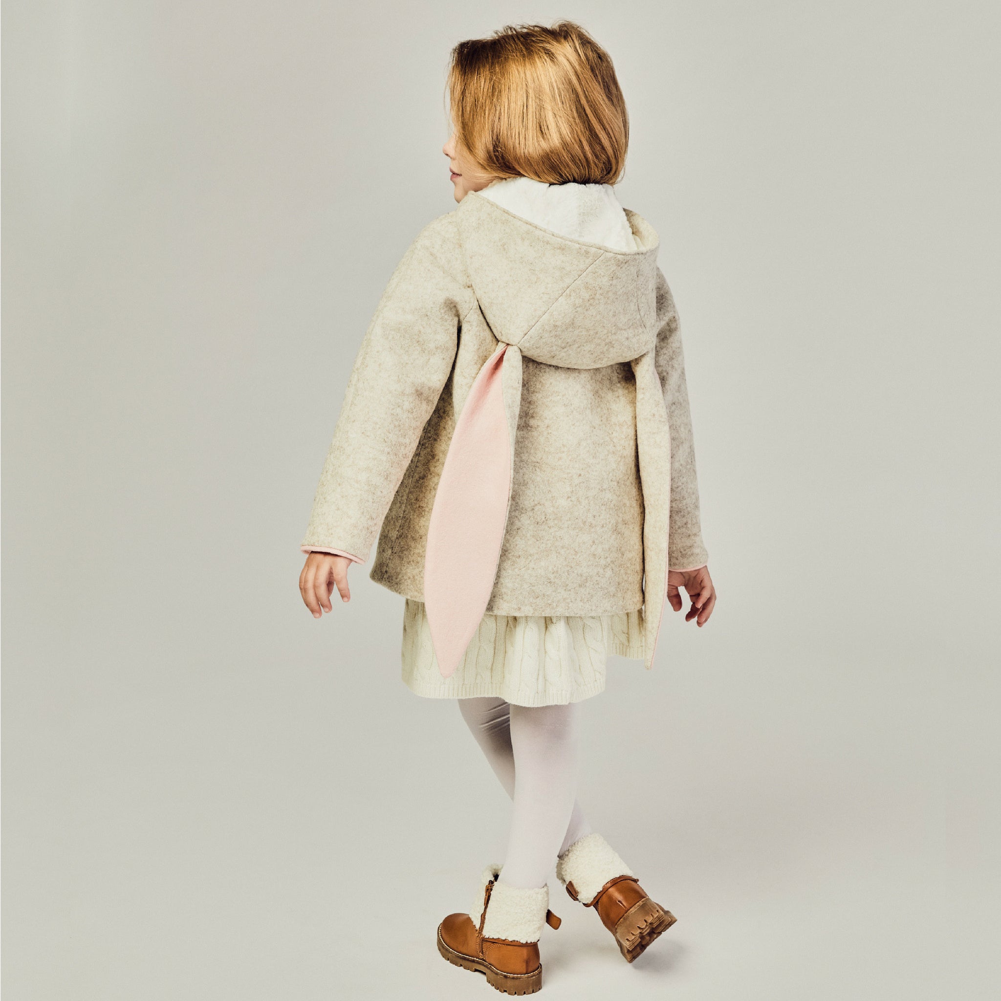 Back view of a child wearing a Snowshoe Rabbit Coat, a merino wool hooded jacket with bunny ears, perfect for winter.