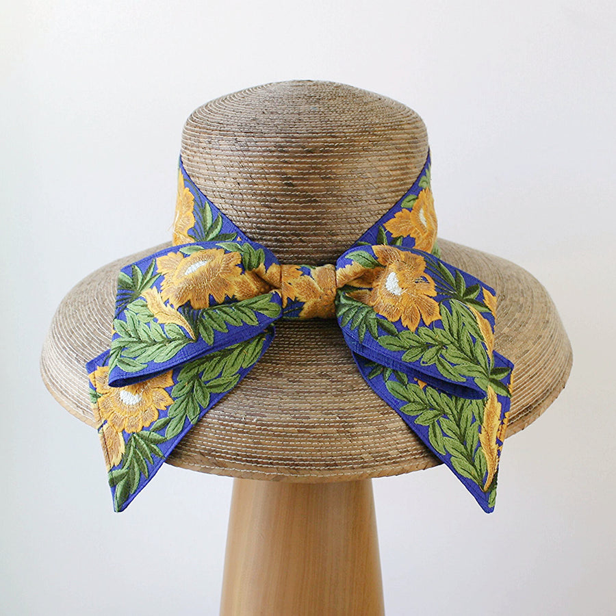 Back view of Audrey Sunflower straw hat featuring oversized French blue embroidered bow with yellow flowers