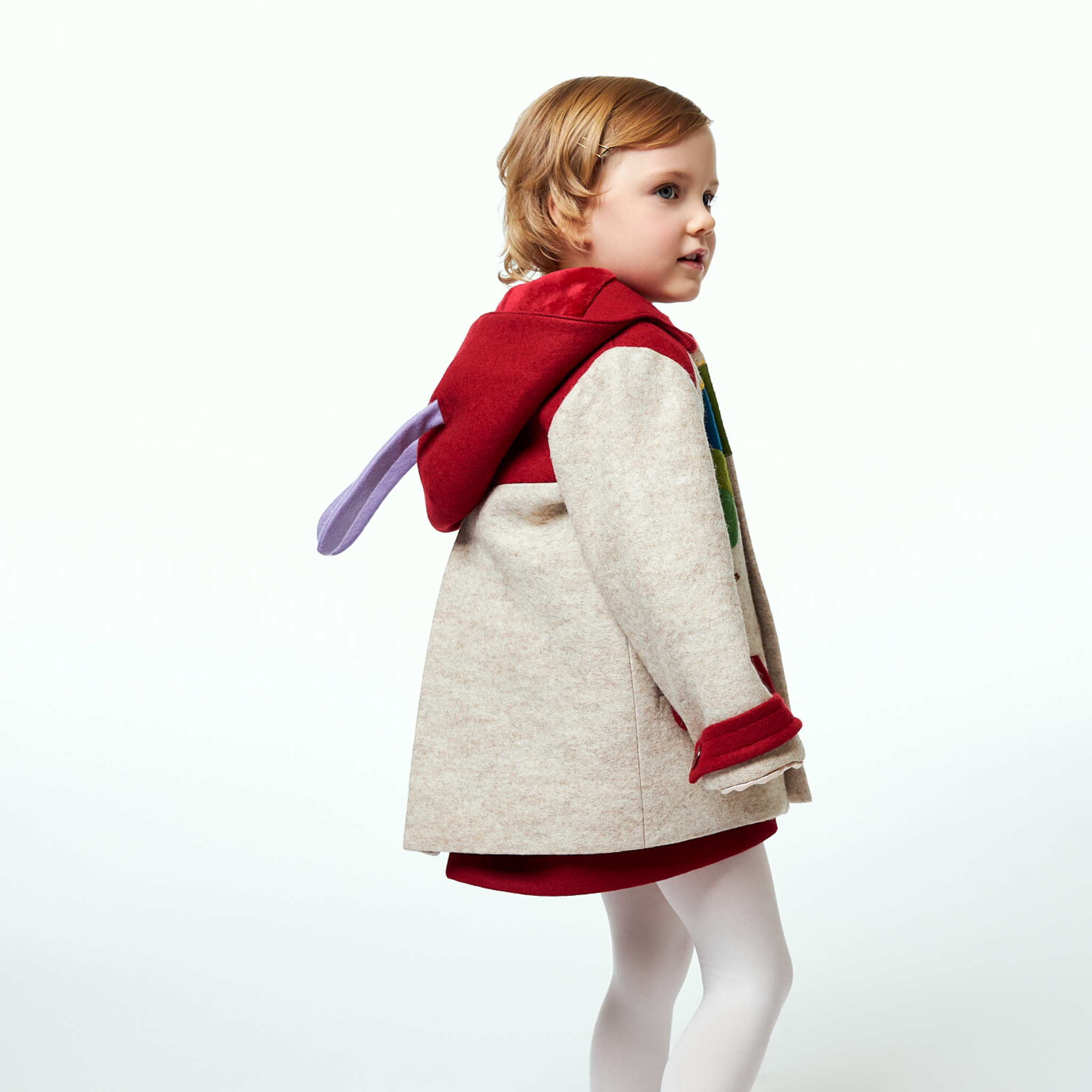 Young girl wearing a Hungry Caterpillar wool coat with red accents and an antennae hood, shown from the back with playful purple antennae detail
