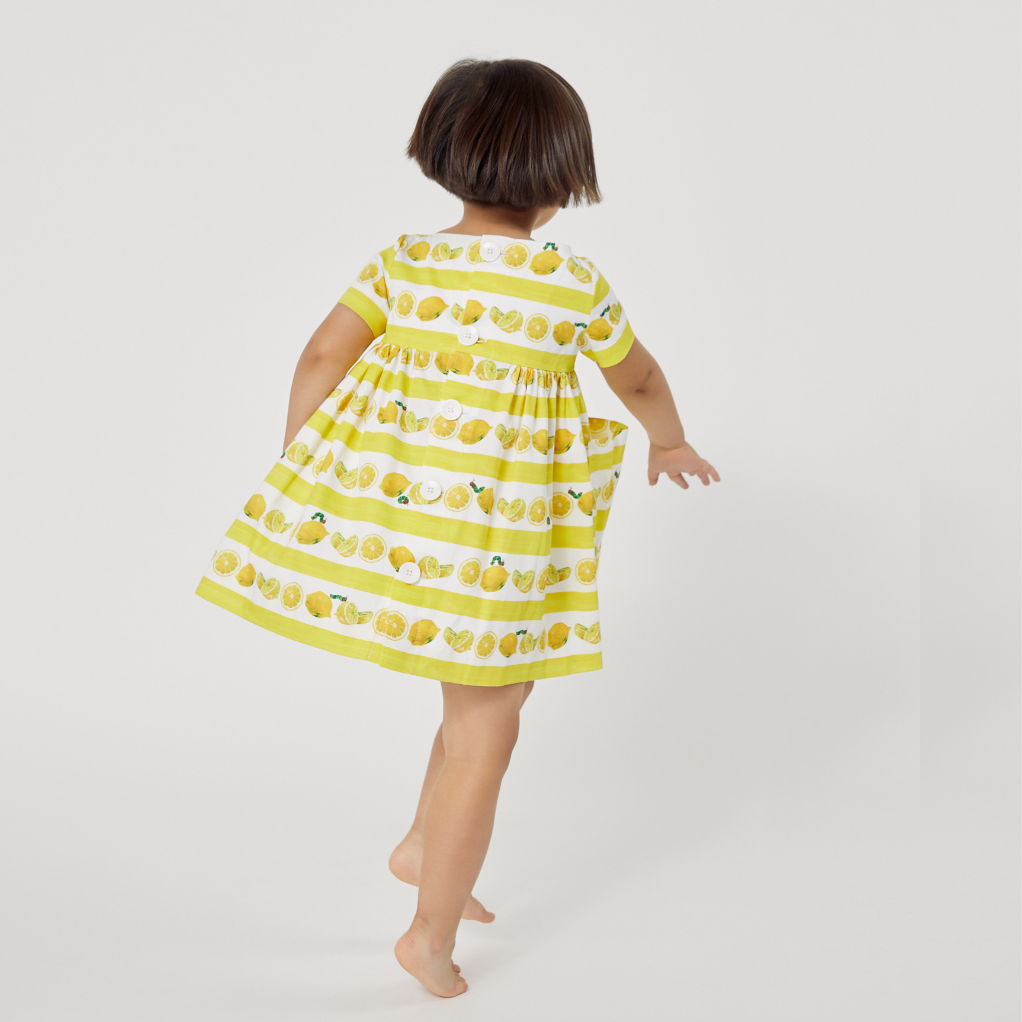 Young girl twirls in a lemon-print dress, showing off its flowy design and playful back view