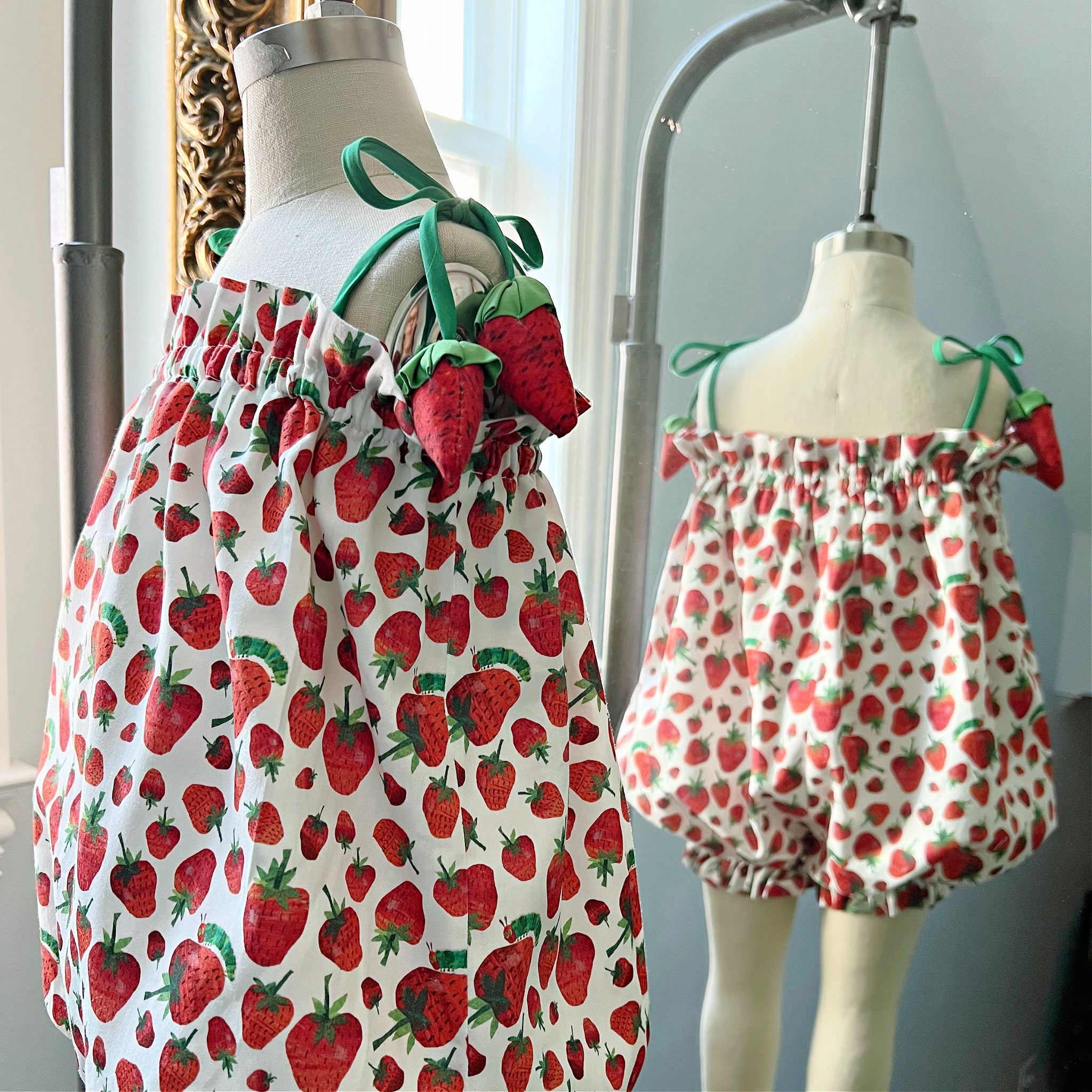 Front and back mannequin display of a strawberry-print bubble romper with adjustable straps