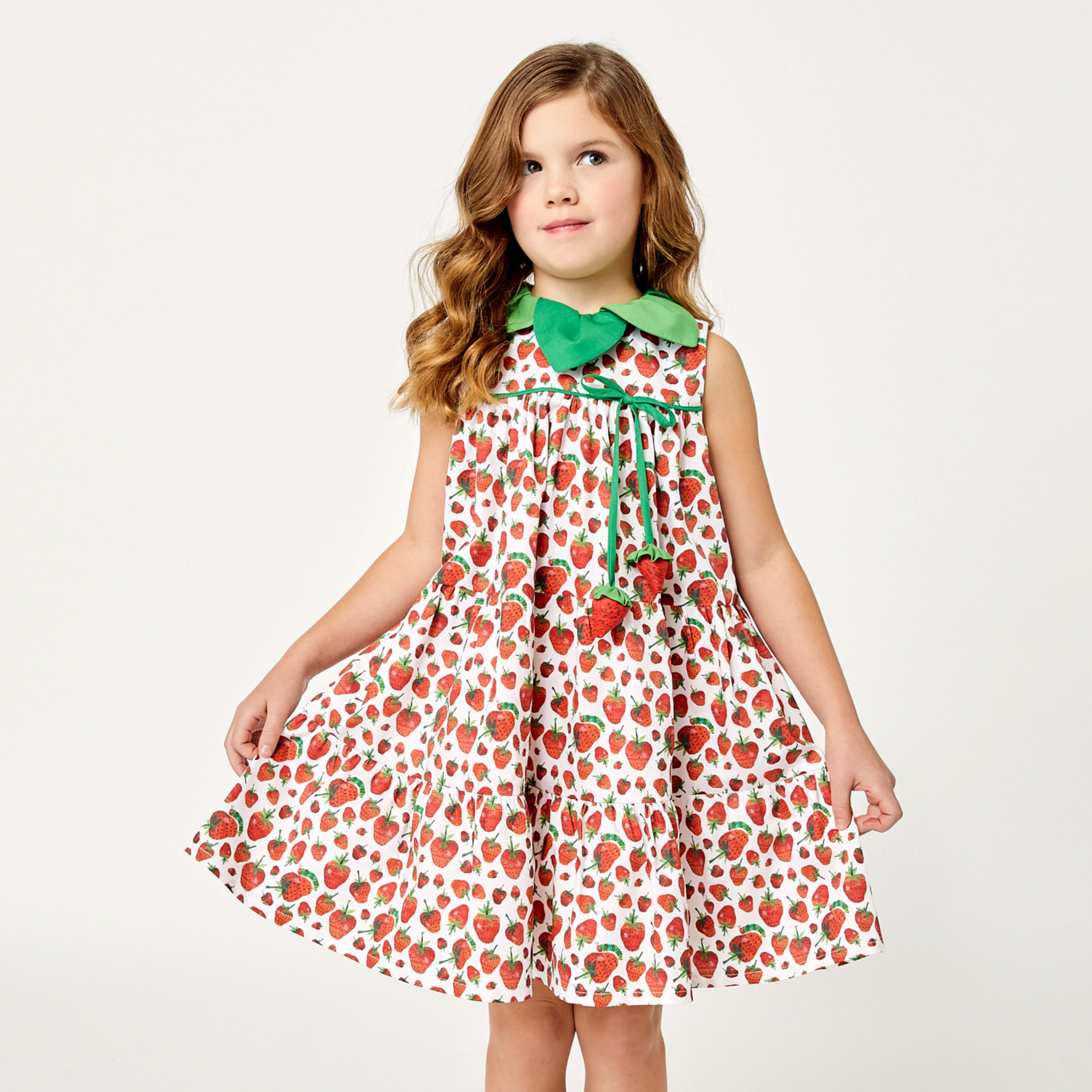 Girl wearing a sleeveless strawberry print dress with a green leaf collar and stuffed strawberry ties, designed for twirling and summer wear