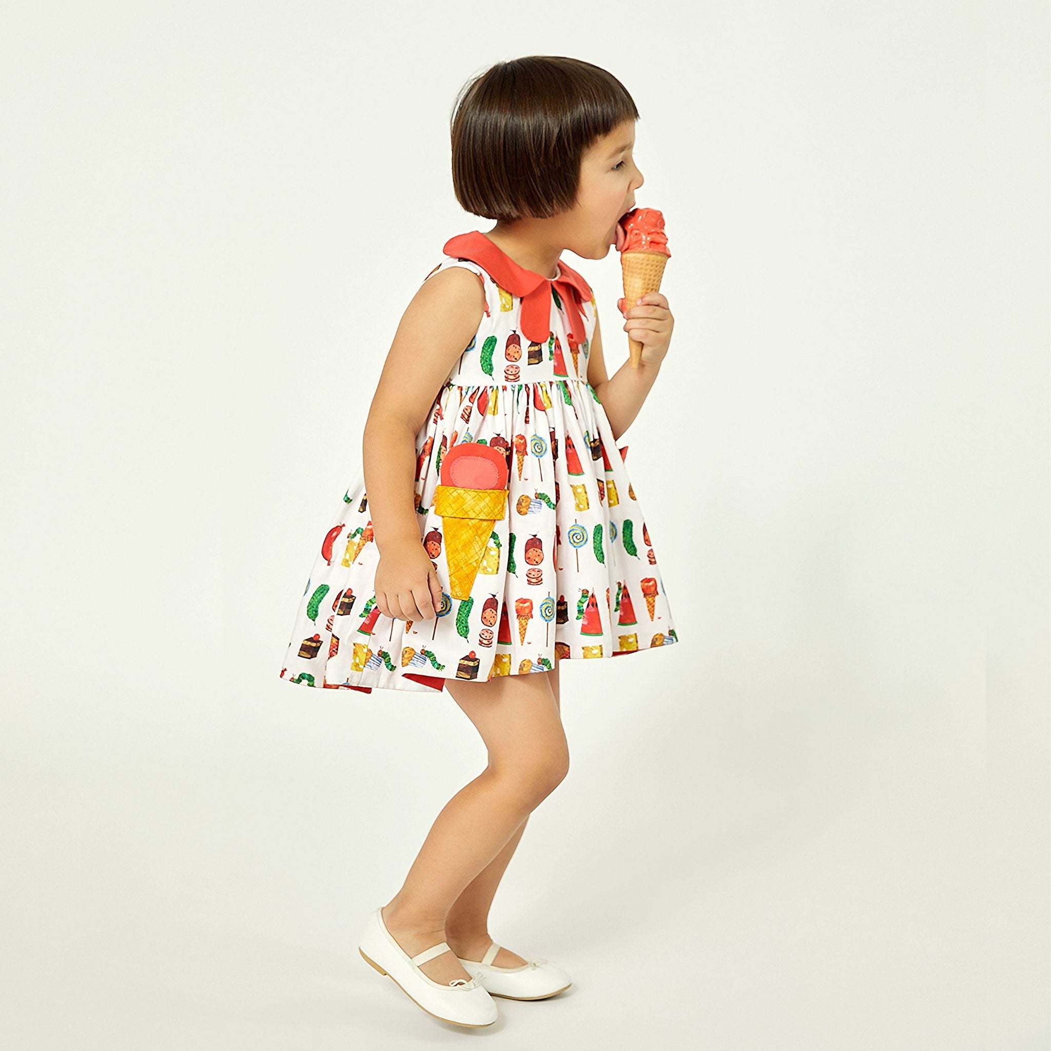 Girl in cotton Two Scoops Dress with ice cream pockets and coral collar, licking an ice cream cone. Playful candy-themed summer outfit for kids.