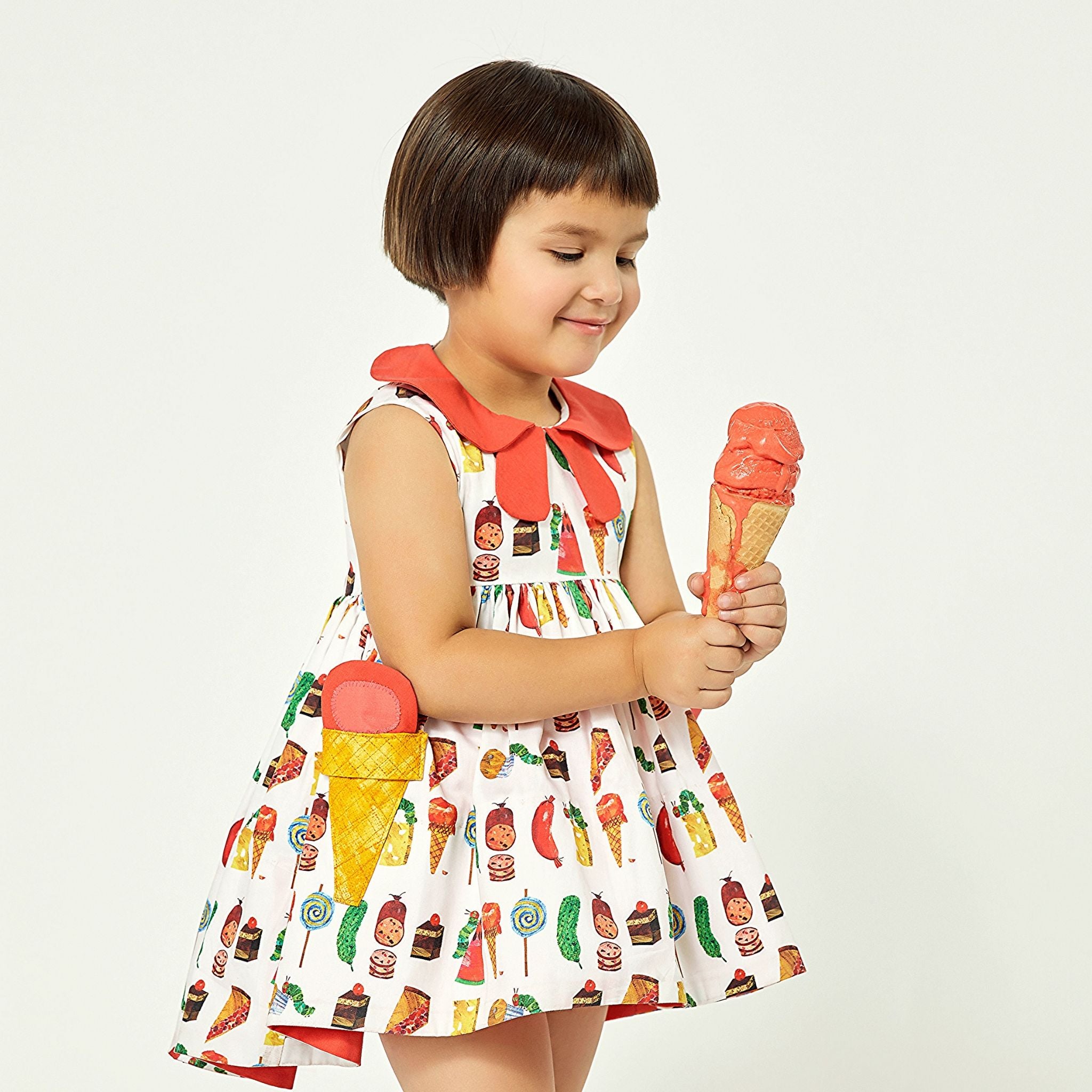 Girl wearing cotton Two Scoops Dress with The Very Hungry Caterpillar print, coral collar, high-low hem, and quilted ice cream cone pockets.
