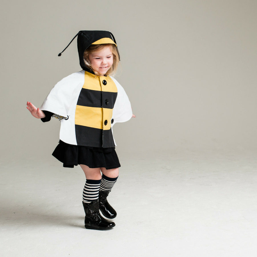 Girl wearing a bumblebee cape with hood and antennae, featuring black and yellow stripes. Playful animal-inspired children's outfi