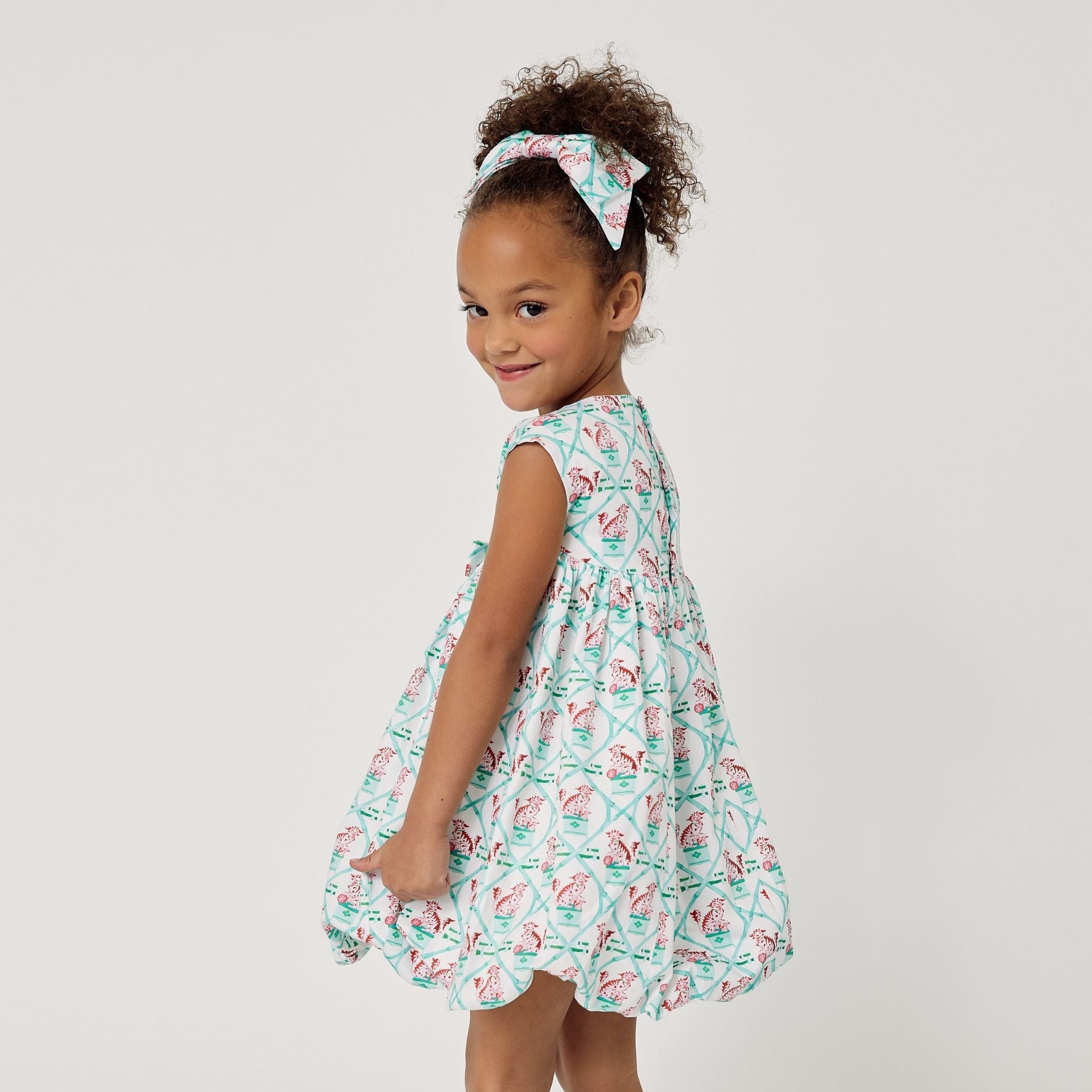 Back view of a girl twirling in a mint carrot-print dress with a gathered waist