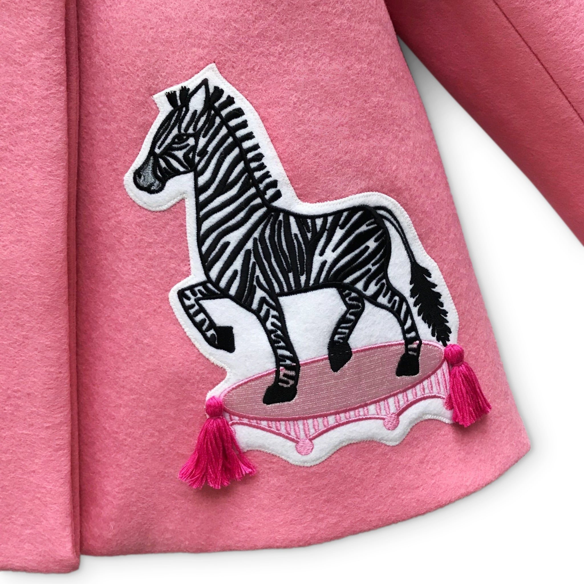 Close-up of zebra appliqué on Yolanda and Tatty pink wool coat, featuring embroidered details and pink tassels.